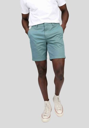 Shorts en coton bleu clair avec une coupe décontractée, poches latérales et devant plat, associés à des baskets montantes blanches.