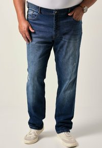 Vaqueros de mezclilla azul oscuro con un ligero desgaste, corte recto, diseño de cinco bolsillos y detalles de costura visibles. Llevados con zapatillas blancas.