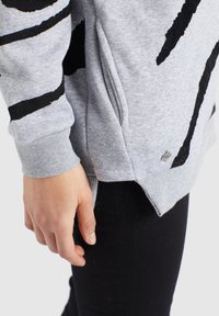 Felpa grigia con motivi astratti neri, polsini a coste e un design con spacco laterale. Abbinata a pantaloni neri aderenti.