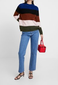 Gruby, wielopasmowy sweter w kolorach niebieskim, czarnym, zielonym, brązowym, różowym i białym; zestawiony z jasnoniebieskimi prostymi jeansami i czerwoną torebką.