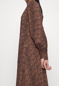 Abito marrone con stampa leopardata nera, maniche lunghe a sbuffo e vestibilità comoda. Il tessuto sembra leggero e presenta una consistenza liscia.