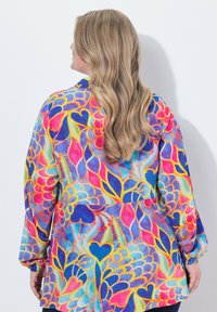 Blusa a maniche lunghe con fantasia floreale colorata, caratterizzata da un orlo curvo e un design vibrante nei toni di blu, rosa e giallo.