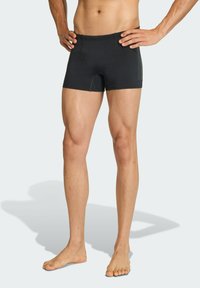 Pantalones cortos deportivos negros hechos de tela elástica, con un diseño ajustado y un panel lateral en contraste. Textura suave con una cinturilla.