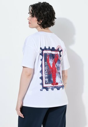 Osoba z krótkimi kręconymi włosami, ubrana w białą koszulkę z dużym czerwonym homarem i napisem „SUMMER” na plecach, w połączeniu z ciemnymi spodniami.