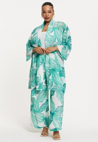 Leichtgewichtiger, transparenter Kimono in Weiß mit grünen, gewellten Blattmustern, kombiniert mit passenden weitgeschnittenen Hosen und einem weißen Oberteil.