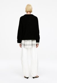 Schwarzer, flauschiger Pullover, darunter ein weißes kariertes Hemd, weiße weit geschnittene Hosen und schwarze Absatzsandalen. Minimalistisches, modernes Design, keine Muster.