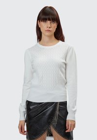 Maglione bianco lavorato a maglia con un motivo a diamante testurizzato sul petto, maniche lunghe e scollatura rotonda abbinato a una gonnella in pelle nera.