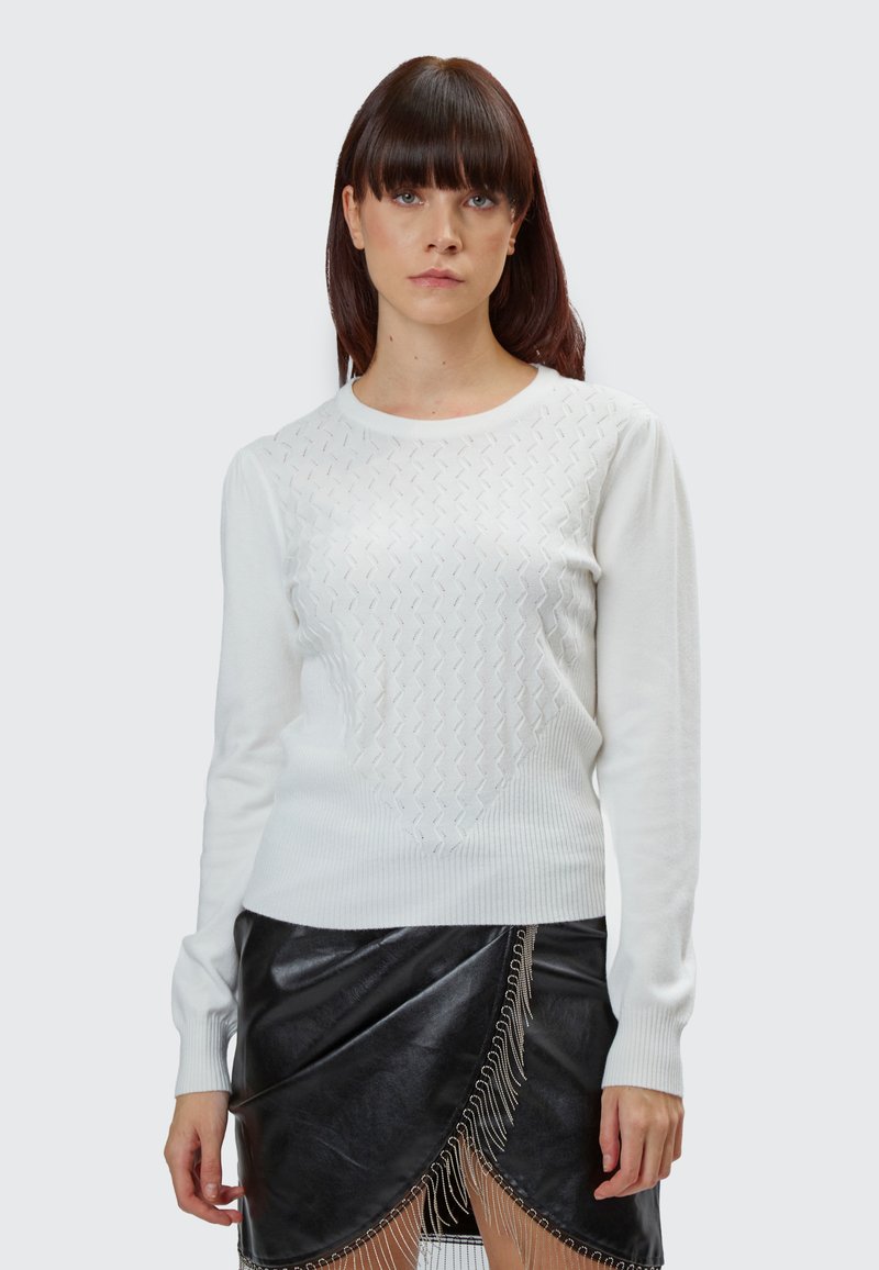 Maglione bianco lavorato a maglia con un motivo a diamante testurizzato sul petto, maniche lunghe e scollatura rotonda abbinato a una gonnella in pelle nera.