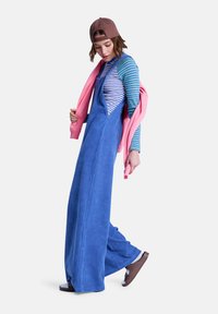 Μπλε σαλοπέτα από κορδόνι με φαρδιά πόδια, φορεμένη πάνω από μια ριγέ μπλούζα με μακριά μανίκια, συμπληρωμένη με ροζ φούτερ που είναι περασμένο στους ώμους.