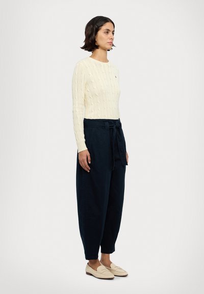Pulover din tricot cu model de cablu de culoare crem, pantaloni navy largi cu talie legată și loferi bej. Design simplu, texturi moi și culori neutre.