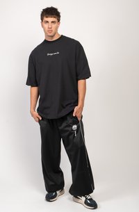 Black oversized t-shirt with white embroidered text and black satin-like wide pants featuring white side stripes and a logo design.