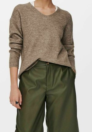 Pull en tricot marron avec un col en V et des manches longues, associé à un pantalon large en cuir vert avec une fermeture à bouton et des plis.
