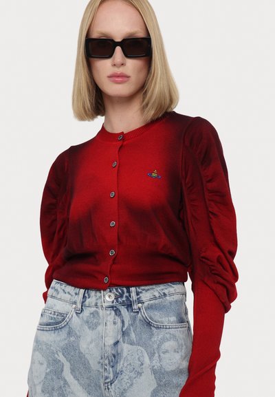 Červený kardigan s nabíranými rukávy, kulatým výstřihem a pěti stříbrnými knoflíky. Nošený s džínami s jasným ombré efektem, které mají zdobený design.