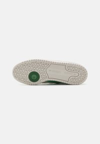 Green sneaker outsole with textured rubber, circular patterns, and a round green accent in the heel area. Brand logo visible.
