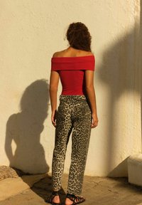 Rode off-the-shoulder geribbelde top gecombineerd met hoge taille luipaardprint jeans en zwarte strapsandalen, gezien van achteren tegen een muur.
