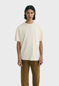Crèmegekleurde crewneck t-shirt van zachte katoen. Korte mouwen en een relaxte pasvorm. Draag het met bruine broeken met cargozakken.