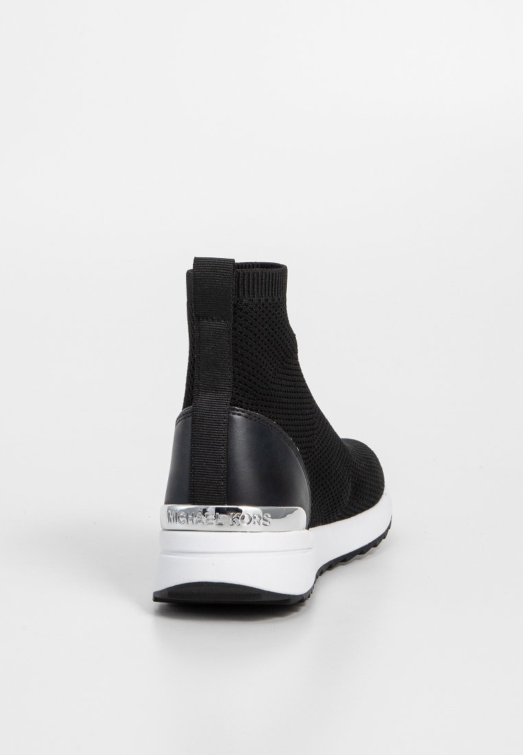 Bottines mules en résille noire au design épuré, avec un côté élastique et un accent de logo métallique sur le talon. Semelle blanche avec un motif texturé.