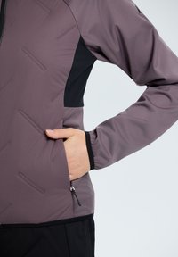 Giacca da esterno in un viola tenue e nero, con una superficie testurizzata, tasca con zip, polsini elastici e un design aderente.