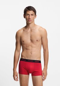 Røde boksershorts lavet af blødt stof med en tætsiddende pasform. Sort linning med "HUGO" i rødt bogstavtryk. Glat tekstur, midt på låret længde.