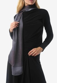 Écharpe ombrée grise en matériau léger, drapée autour du cou, avec une texture douce et un léger éclat, associée à une robe noire ajustée.