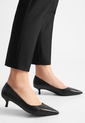 Zapatos de tacón alto de cuero negro con punta puntiaguda y tacón bajo tipo kitten, con acabado suave y diseño sutil con recortes.