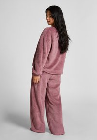 Gezellige, overgrote roze fleece loungewear set bestaat uit een longsleeve top en wijde broekspijpen met een zachte, textuurige afwerking.