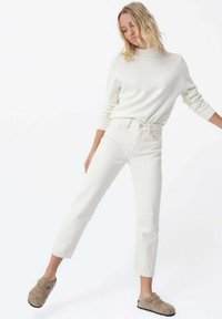 Suéter de algodón ajustado de color claro con puños acanalados, combinado con jeans blancos de pierna recta de cintura alta y zapatos de lona beige.