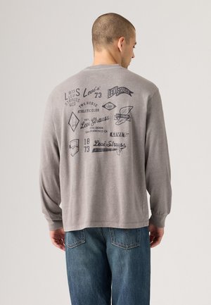 Gray long-sleeve shirt with printed black graphics, featuring logos and text related to Levi's. Simple crew neckline and straight hem.