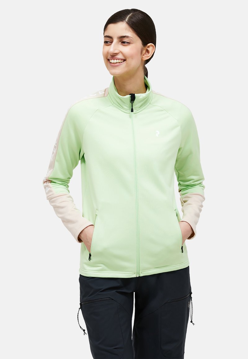 Hellegrüne Zip-Jacke mit hohem Kragen, kontrastierenden beigefarbenen Ärmeln, Seitentaschen und einem dezenten Logo auf der oberen linken Brust.