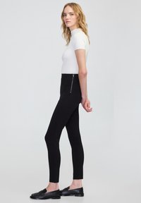 Czarne legginsy z wysokim stanem o gładkim wykończeniu, z bocznym zamkiem błyskawicznym. Połączone z dopasowaną, białą bluzką z krótkim rękawem i czarnymi mokasynami.