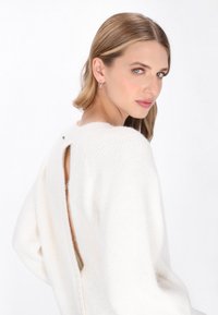 Biały, teksturowany sweter z wycięciem na plecach i guzikami. Posiada długie rękawy i miękki, dzianinowy materiał. Czysty i minimalistyczny design.