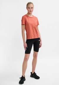 Kortærmet koralfarvet t-shirt med rund hals, parret med sorte cykelsort. Sorte sneakers fuldender sætningen.