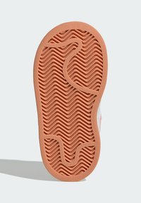 Guma podošvy detskej obuvi svetlohnedej farby so vzorom s cik-cakovými a zakrivenými drážkami na svetlosivej pozadí.