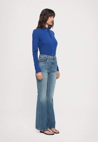 Långärmad blå skjorta med knappar i kombination med ljusblå utsvängda jeans. Skjortan är skräddarsydd och jeansen är i mellanblå denim med en lätt blekning.