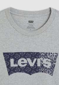 Pilkas medvilninis marškinėliai su tamsiai mėlynu grafiniu logotipu, gėlėmis, su apvalia kaklo iškirpte ir standartiniu sijonu. Etiketas matomas viduje.