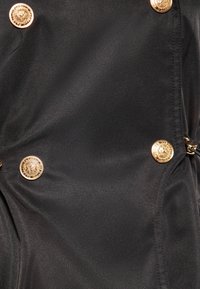 Zwarte stoffen kleding met decoratieve knopen in goudtint, met een gladde textuur en een getailleerd ontwerp. Opvallend detail: geplooide stofsecties.