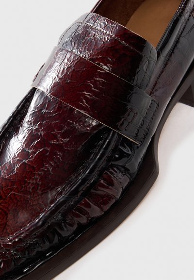 Glossy dark burgundy leather loafer with textured finish, moc toe stitching, and a broad strap across the vamp on a low heel.