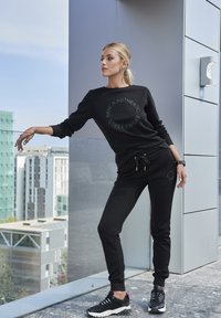 Schwarz sweatshirt und Jogginghose mit "Bench Authentic Streetwear" Druck, aus Baumwolle, lässige Passform, mit Kordeln verziert, kombiniert mit schwarzen Turnschuhen.