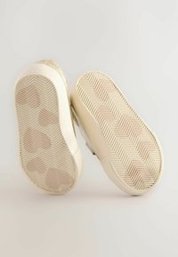 Baskets scintillantes dorées avec une semelle en caoutchouc blanc texturé, présentant un motif en chevrons. La vue arrière met en avant les accents métalliques brillants.