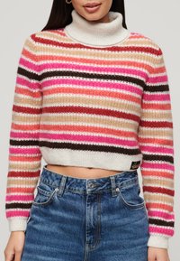 Pull rayé avec col roulé dans des tons de rose, rouge, beige et marron. Tissu tricoté avec un design court et des poignets côtelés.