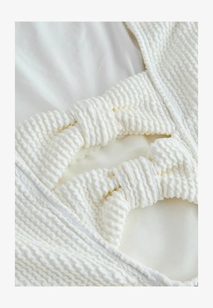 Costum de baie de culoare crem, dintr-un material texturat cu accente plisate și detaliu cu nod, conceput cu margini netede și întindere minimă.