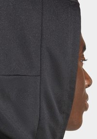 Un sweat à capuche noir avec une surface texturée, doté d'une grande capuche attachée, vu de côté, mettant en évidence la couture et le détail du tissu.