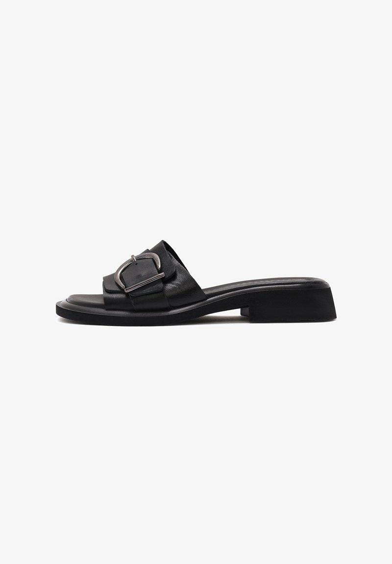 Sandale noire en cuir à enfiler avec une large bride, une grande boucle argentée, un petit talon carré et un bout carré sur fond blanc.