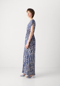 Robe maxi avec un motif en vagues bleu et crème, manches courtes, taille cintrée et tissu doux. Associée à des sandales à talons blocs bleu clair.