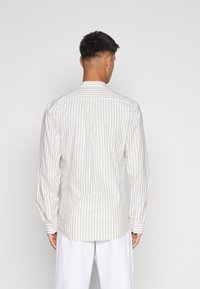 Striped button-up shirt in cream and light brown, featuring long sleeves, a collar, and a curved hem. Material appears lightweight and breathable.