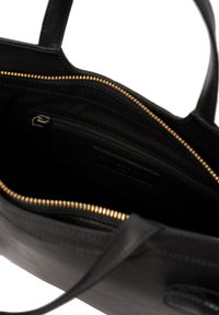Bolso tote de cuero negro con detalles de cremallera dorada, que cuenta con un interior de tela, bolsillo con cremallera y asas planas. Diseñado para un fácil acceso.