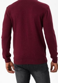 Suéter de punto burdeos visto desde la espalda, con mangas largas, puños y dobladillo acanalados, y una textura suave. Combinado con jeans oscuros.