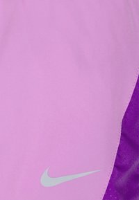 Nike urheilushortsit kirkkaan pinkkinä, sileällä pinnalla. Varustettu hopeisella logolla ja kontrastisilla violetilla verkkosivuosilla.