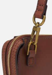 Sac en cuir marron avec une fermeture éclair dorée, des coutures détaillées et un fermoir en métal. La bandoulière a une texture lisse et une boucle solide.