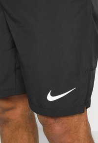 Svarta atletiska shorts med en slät yta. Har en vit Nike-logotyp på vänster fåll. Designen inkluderar sidoklipp för rörelsefrihet.